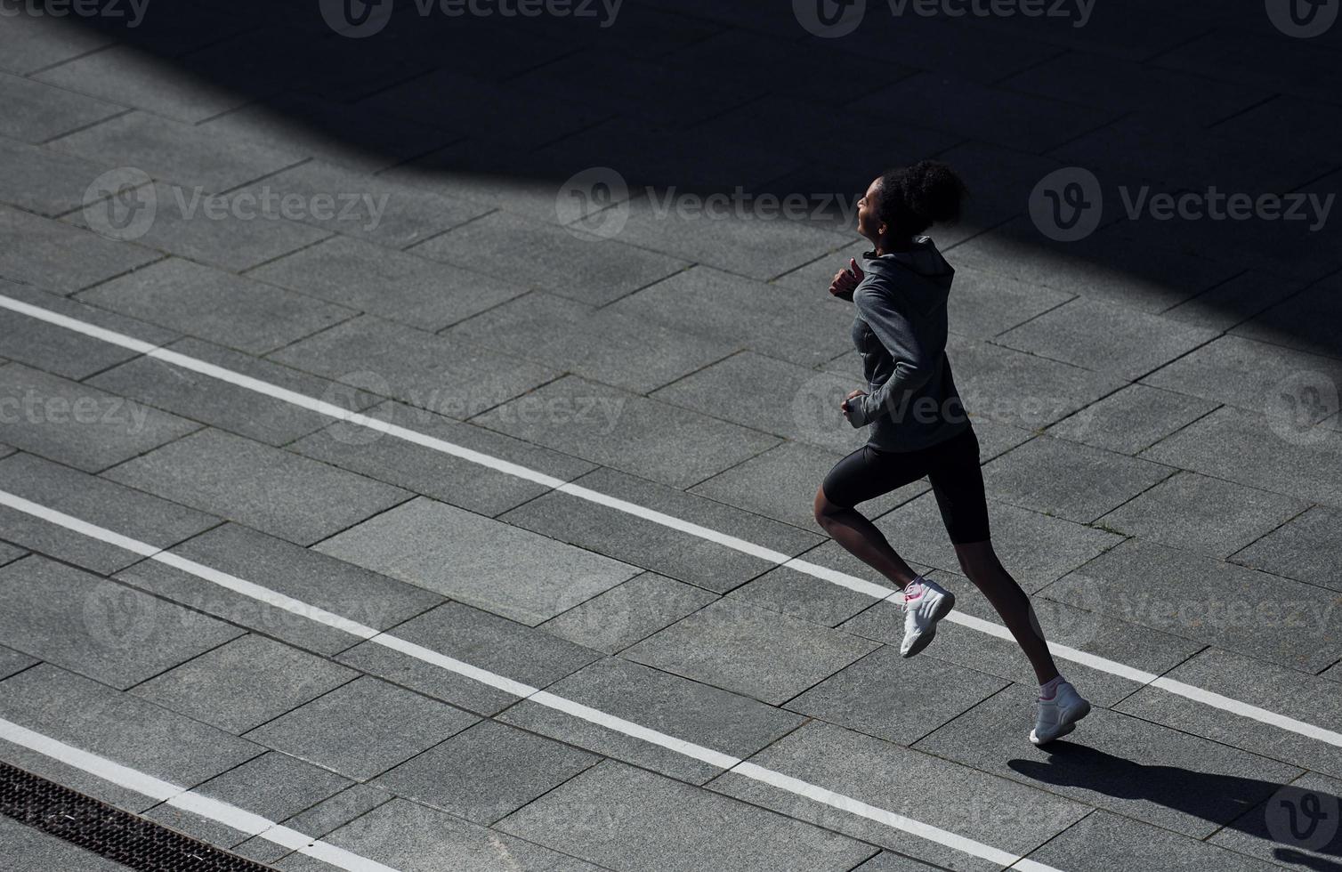 coureur rapide. une jeune femme afro-américaine en vêtements sportifs s'entraîne à l'extérieur pendant la journée photo