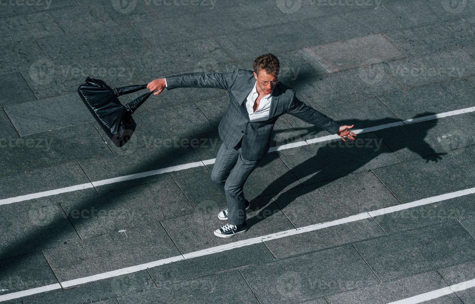 danser, célébrer le succès. jeune homme d'affaires en tenue de soirée grise est à l'extérieur de la ville photo