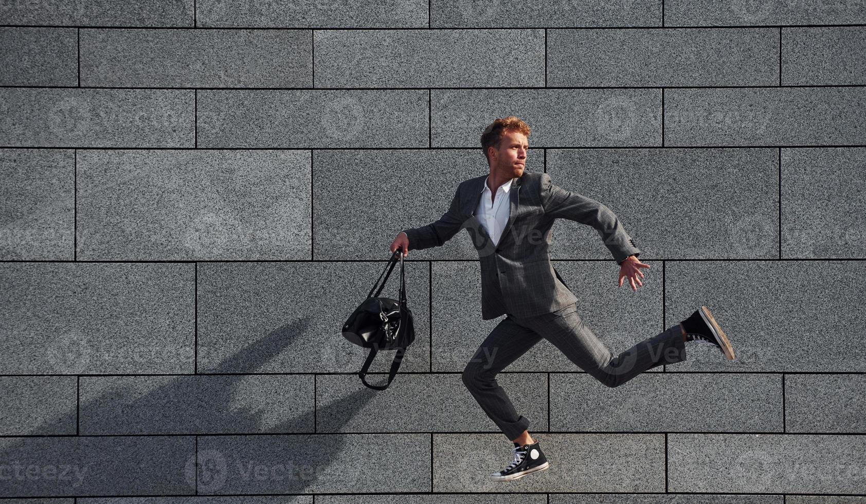 courses et lating au travail. jeune homme d'affaires en tenue de soirée grise est à l'extérieur de la ville photo