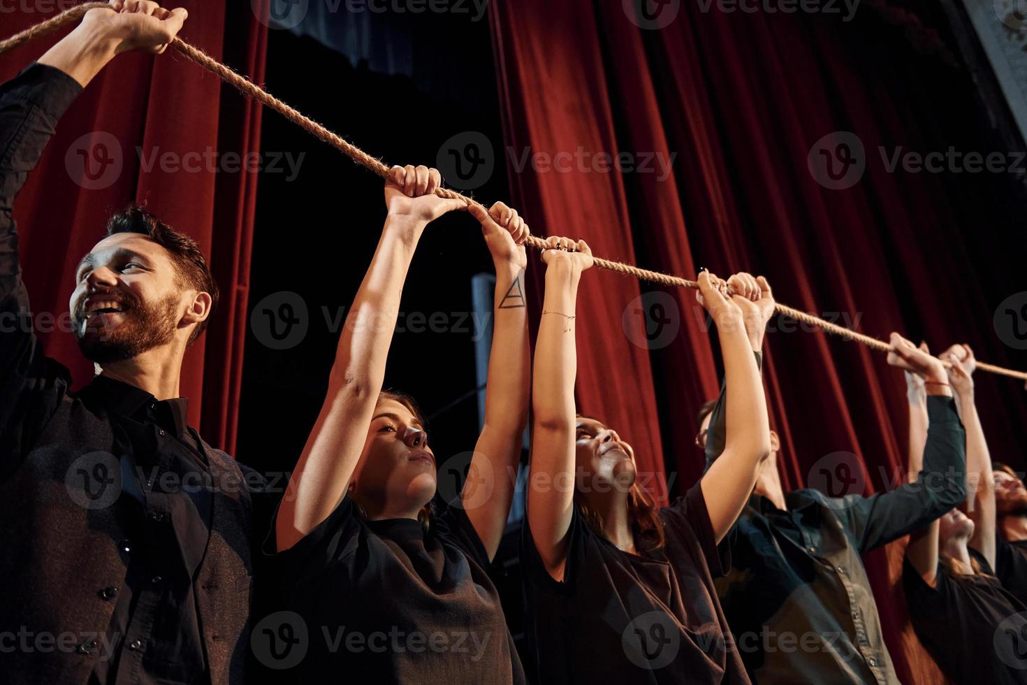 tenant la corde dans les mains au-dessus des têtes. groupe d'acteurs vêtus de vêtements de couleur sombre en répétition au théâtre photo