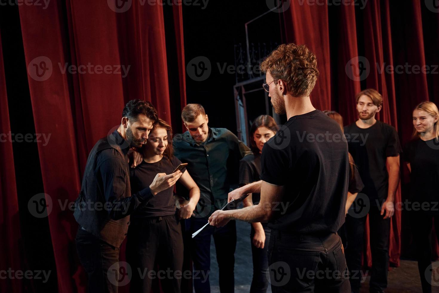 homme avec bloc-notes pratique son rôle. groupe d'acteurs vêtus de vêtements de couleur sombre en répétition au théâtre photo