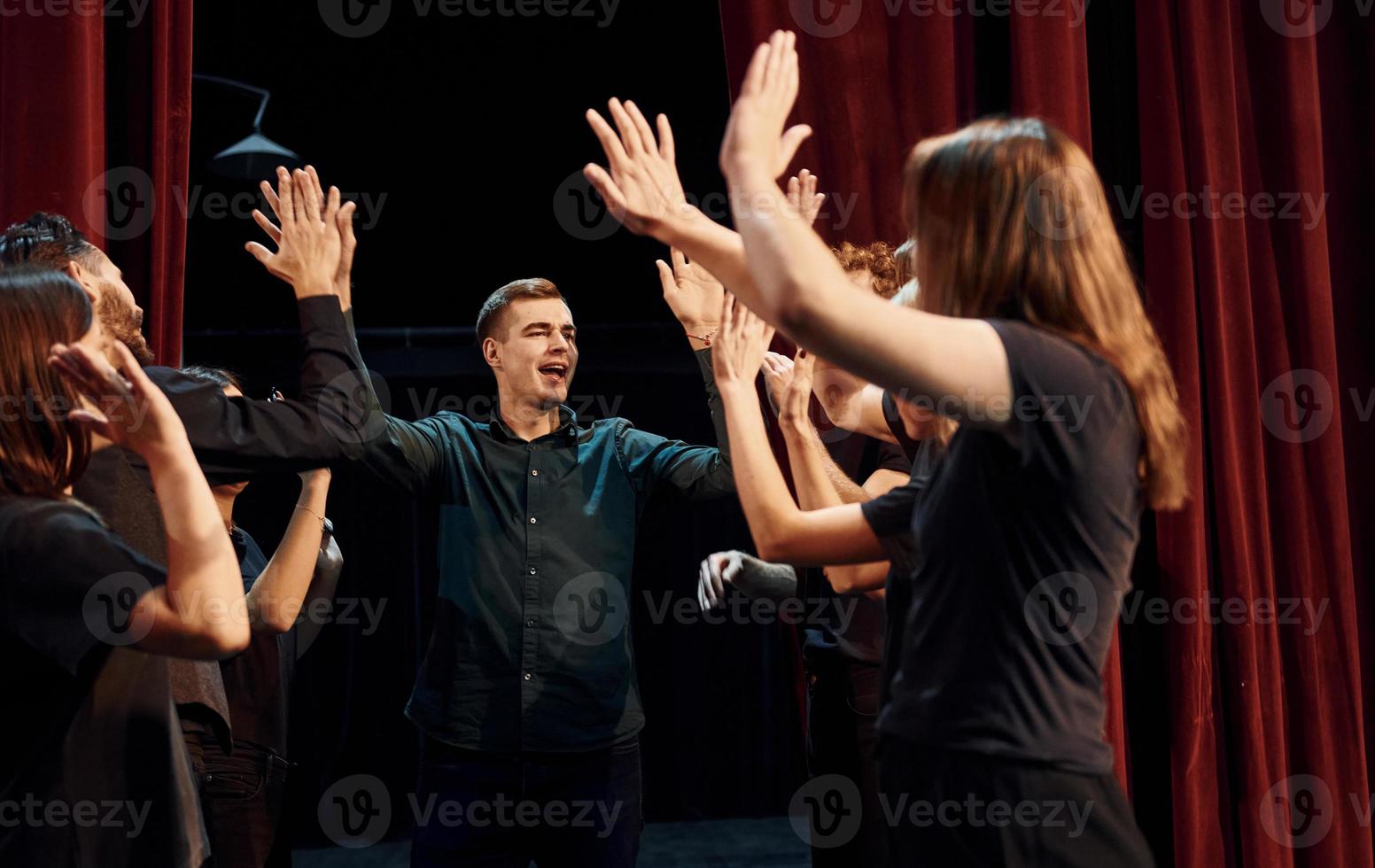 donner un high five, célébrer le succès. groupe d'acteurs vêtus de vêtements de couleur sombre en répétition au théâtre photo