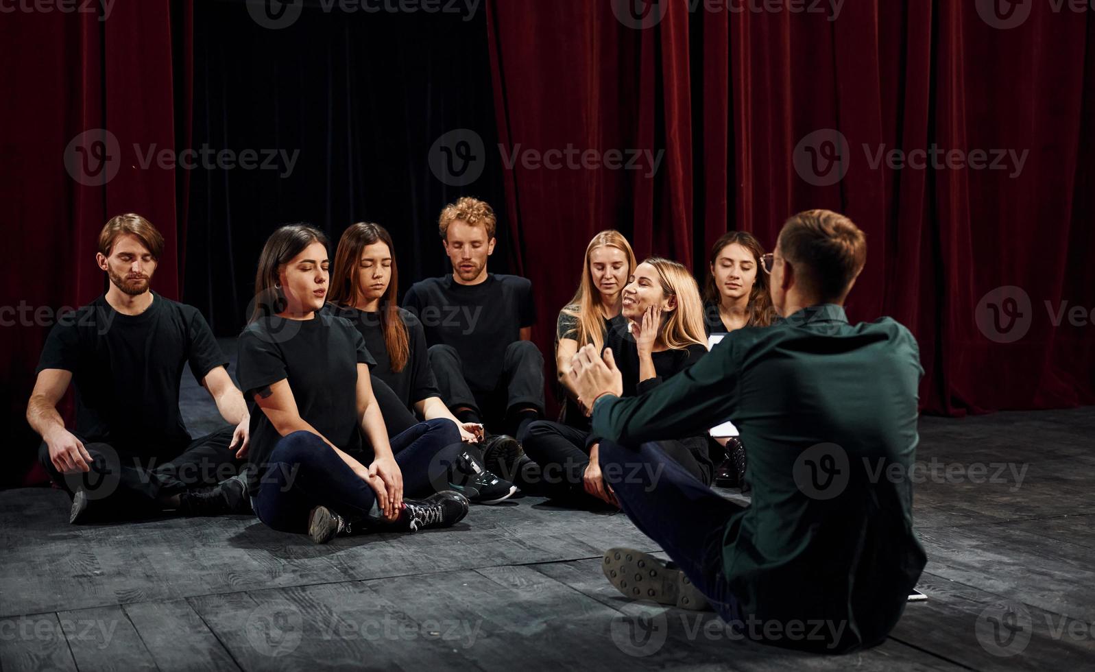 assis sur le sol. groupe d'acteurs vêtus de vêtements de couleur sombre en répétition au théâtre photo