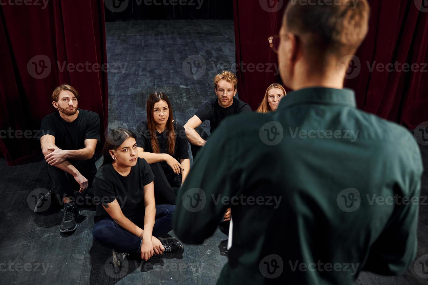 assis et écoutant l'homme. groupe d'acteurs vêtus de vêtements de couleur sombre en répétition au théâtre photo