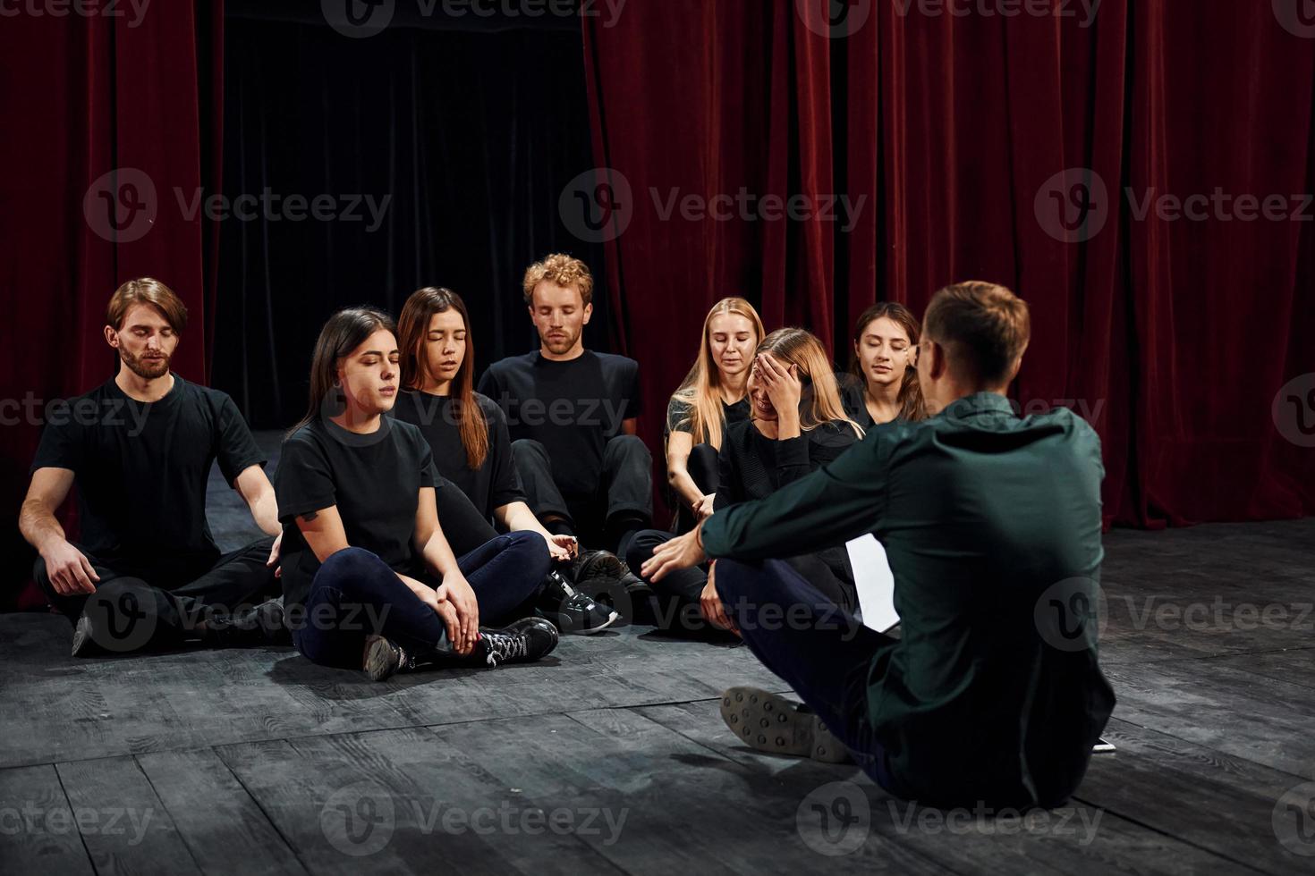 assis sur le sol. groupe d'acteurs vêtus de vêtements de couleur sombre en répétition au théâtre photo