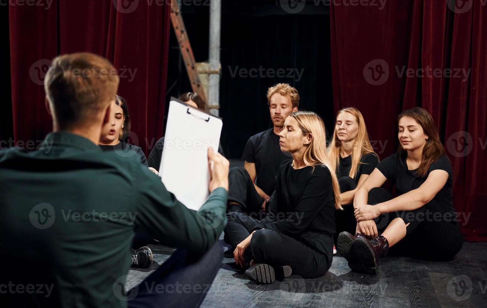 assis sur le sol. groupe d'acteurs vêtus de vêtements de couleur sombre en répétition au théâtre photo