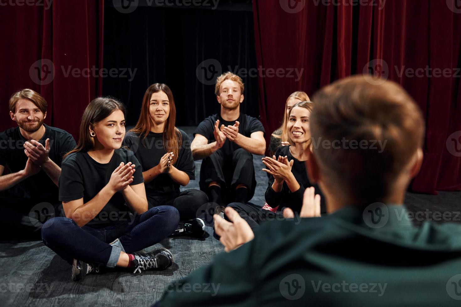 assis sur le sol. groupe d'acteurs vêtus de vêtements de couleur sombre en répétition au théâtre photo