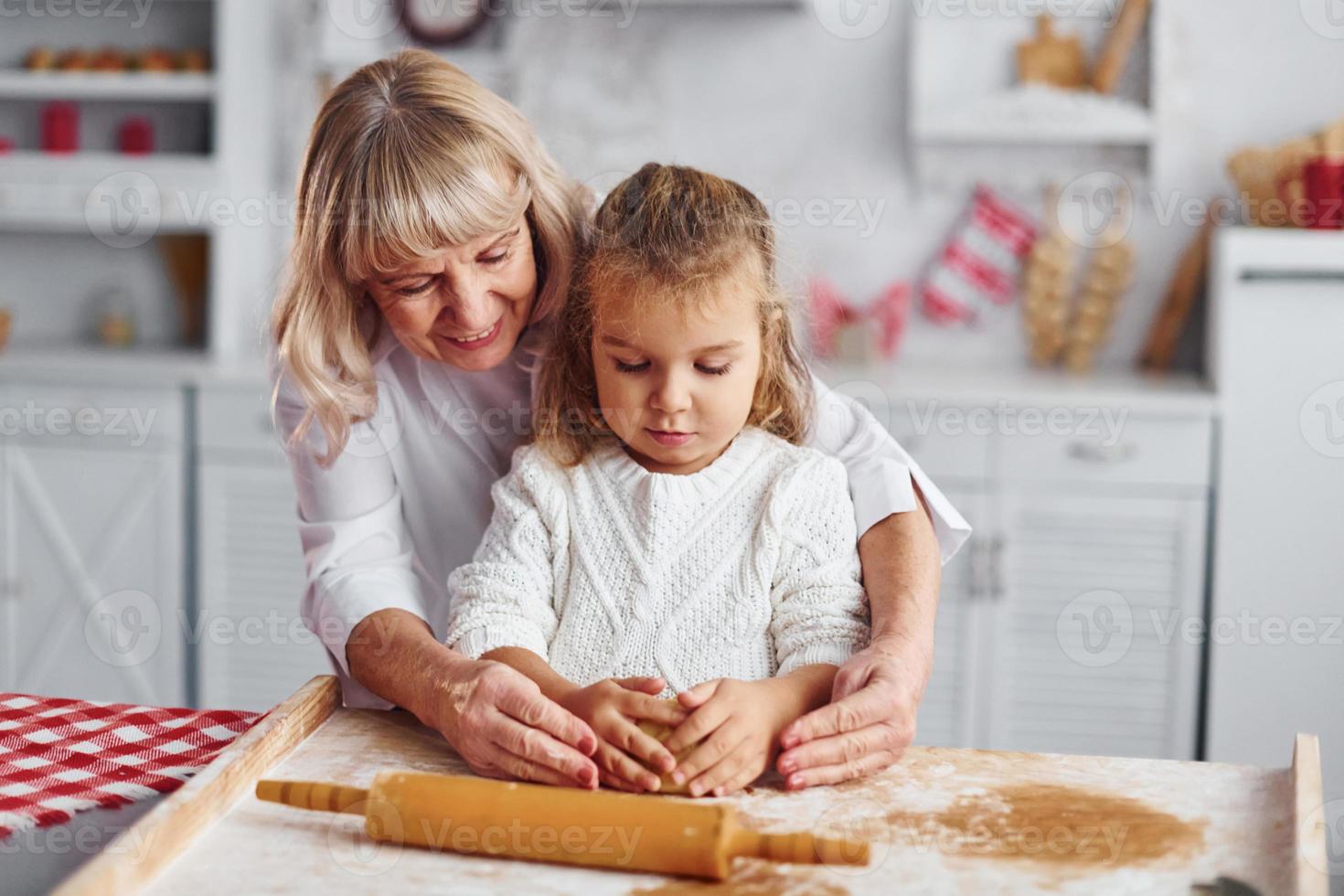 pétrit la pâte. grand-mère senior avec sa petite petite-fille prépare des bonbons pour noël dans la cuisine photo