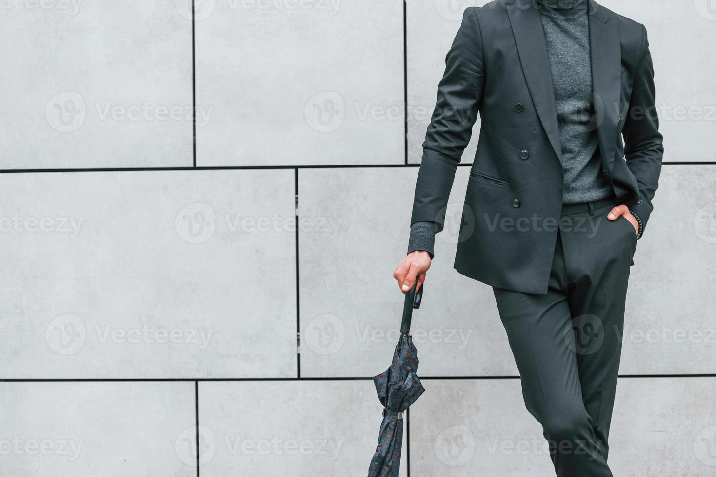 jeune homme en vêtements formels avec parapluie debout près du mur à l'extérieur avec parapluie photo