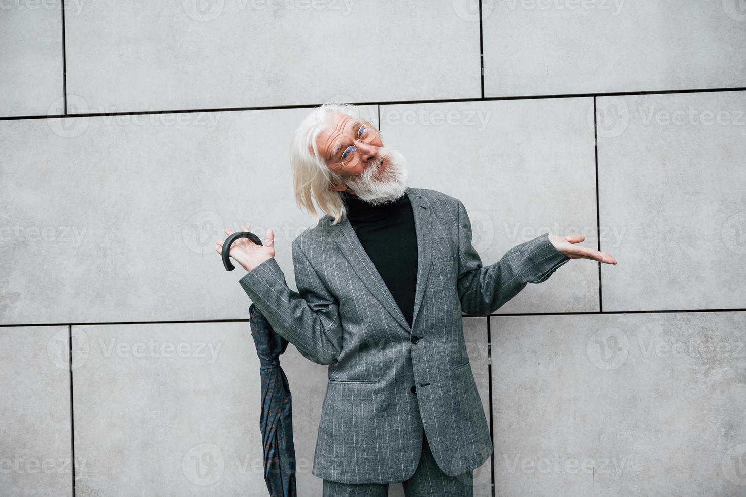 tient un parapluie. homme d'affaires senior en vêtements formels, aux cheveux gris et à la barbe est à l'extérieur photo