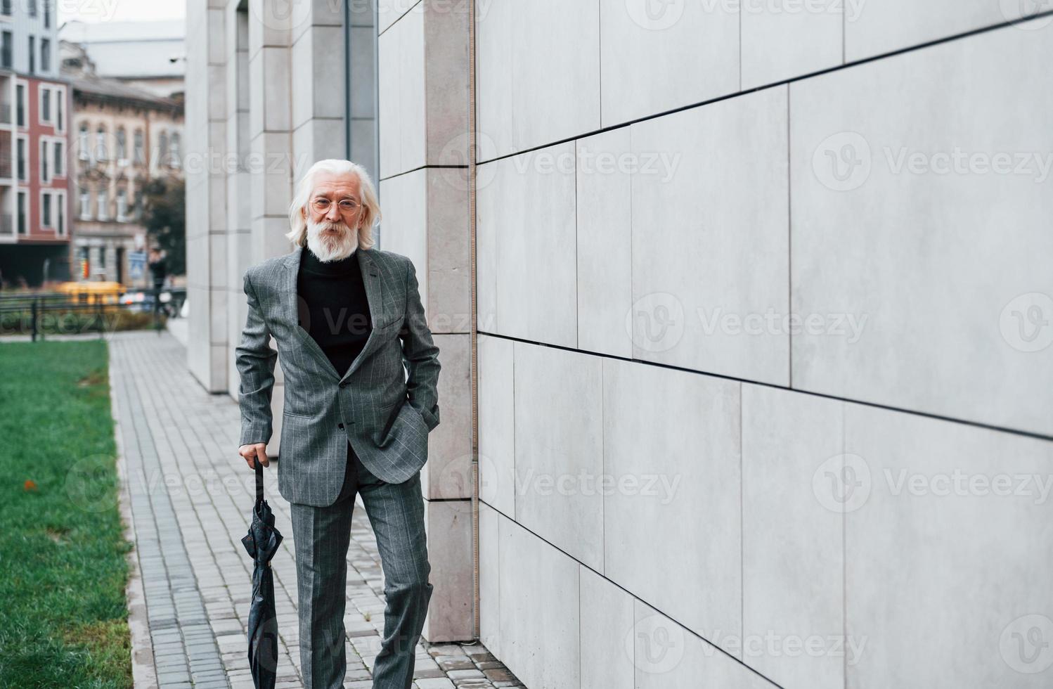 tient un parapluie. homme d'affaires senior en vêtements formels, aux cheveux gris et à la barbe est à l'extérieur photo