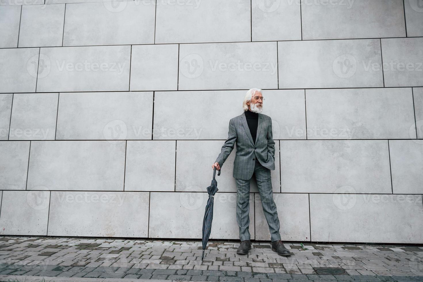 tient un parapluie. homme d'affaires senior en vêtements formels, aux cheveux gris et à la barbe est à l'extérieur photo