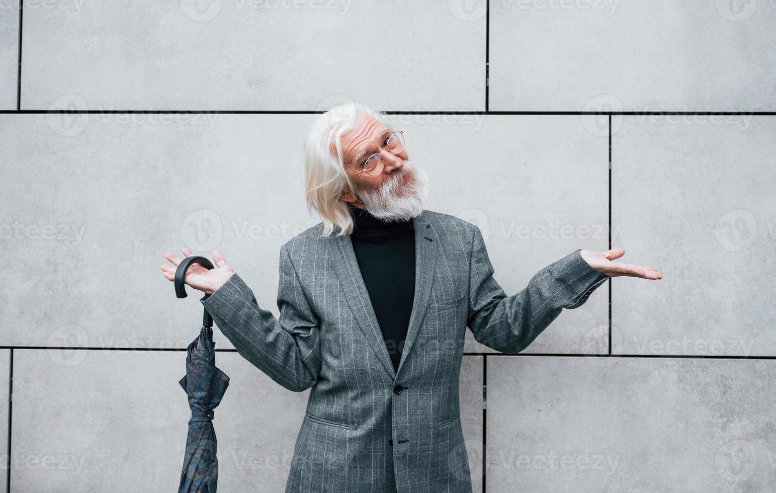 tient un parapluie. homme d'affaires senior en vêtements formels, aux cheveux gris et à la barbe est à l'extérieur photo