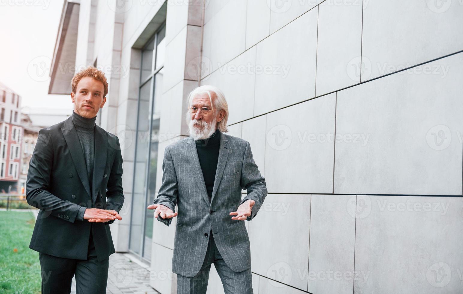 jeune homme avec un homme âgé dans des vêtements élégants est à l'extérieur ensemble. conception d'entreprise photo