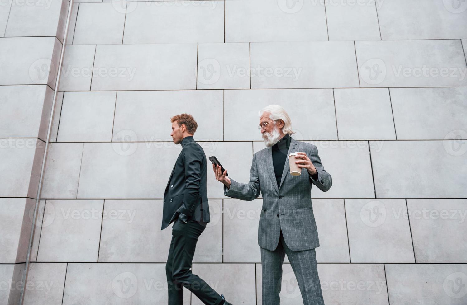 jeune homme avec un homme âgé dans des vêtements élégants est à l'extérieur ensemble. conception d'entreprise photo