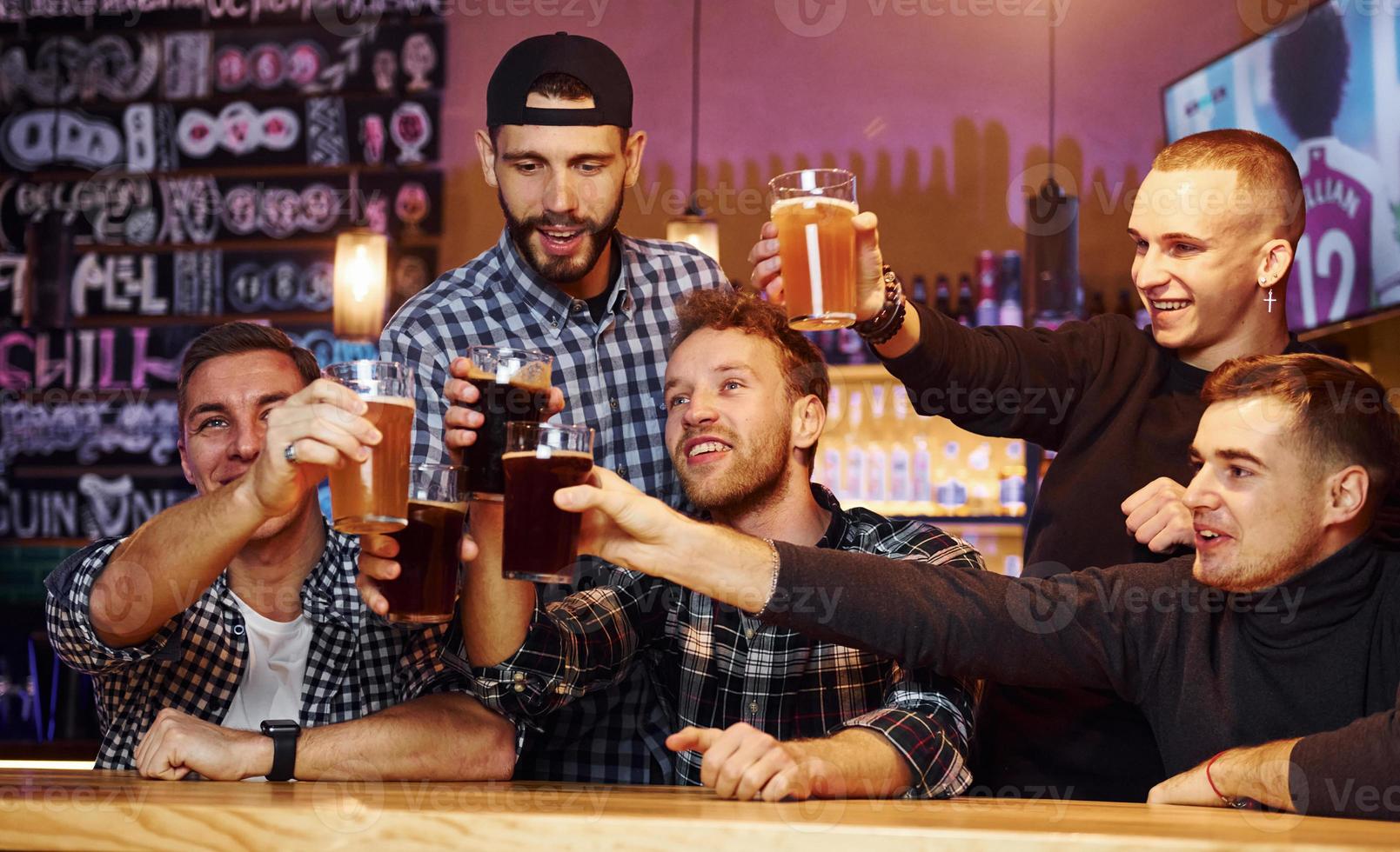 acclamant en frappant des verres à bière. groupe de personnes ensemble à l'intérieur dans le pub s'amuser le week-end photo