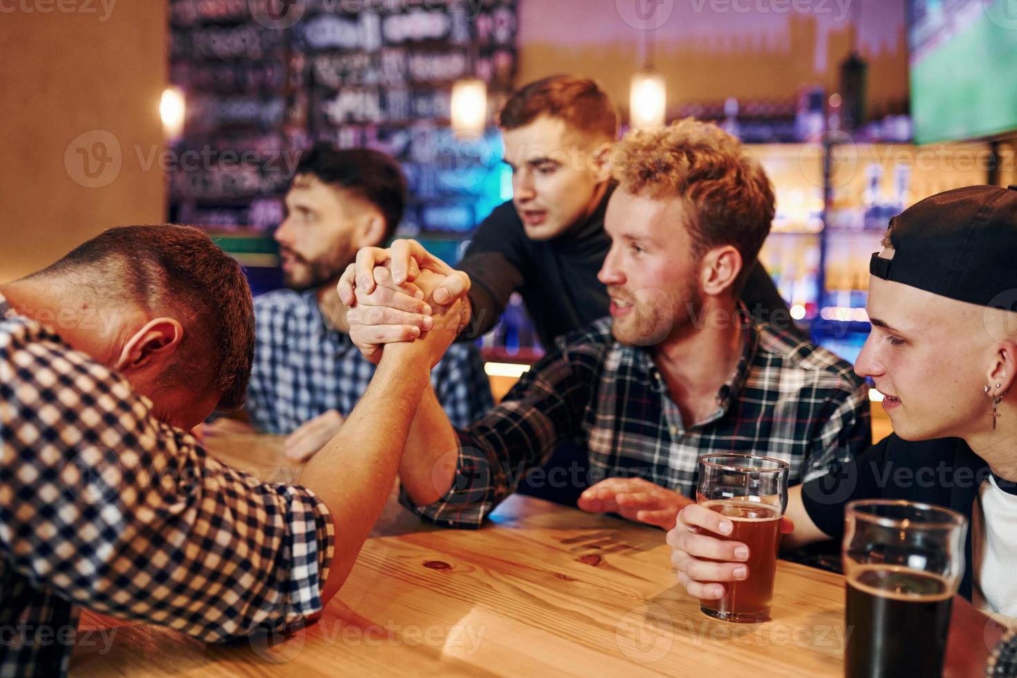 des amis jouent au bras de fer. groupe de personnes ensemble à l'intérieur dans le pub s'amuser le week-end photo