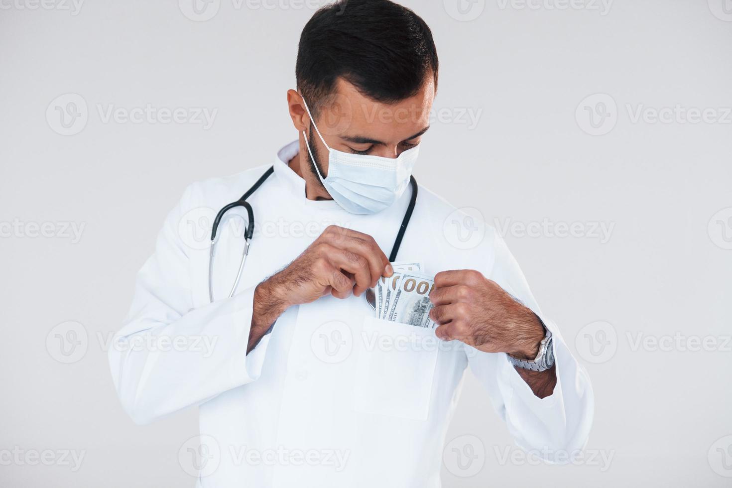 le médecin détient de l'argent. jeune bel homme debout à l'intérieur sur fond blanc photo