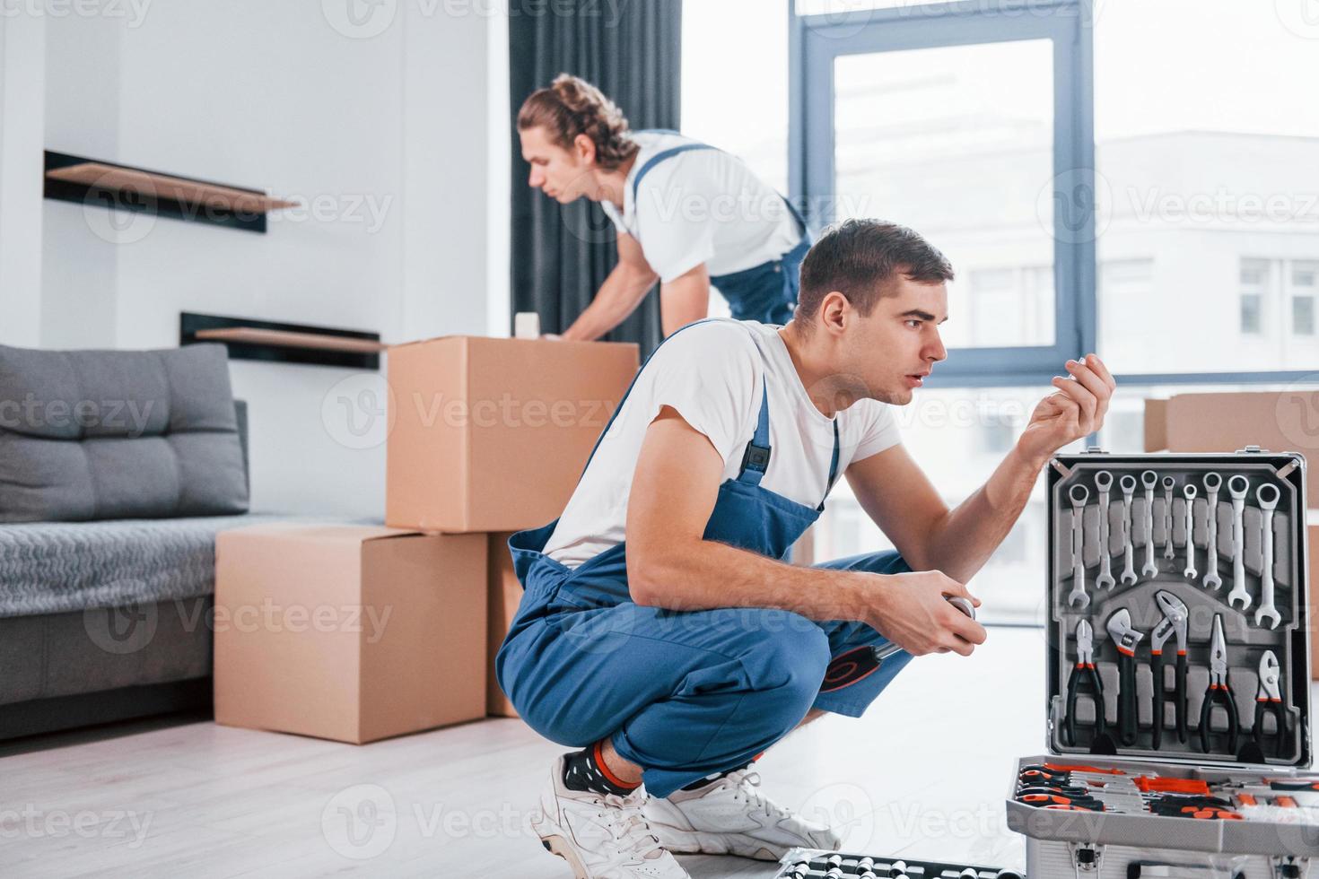 utilise des outils de cas. deux jeunes déménageurs en uniforme bleu travaillant à l'intérieur dans la chambre photo