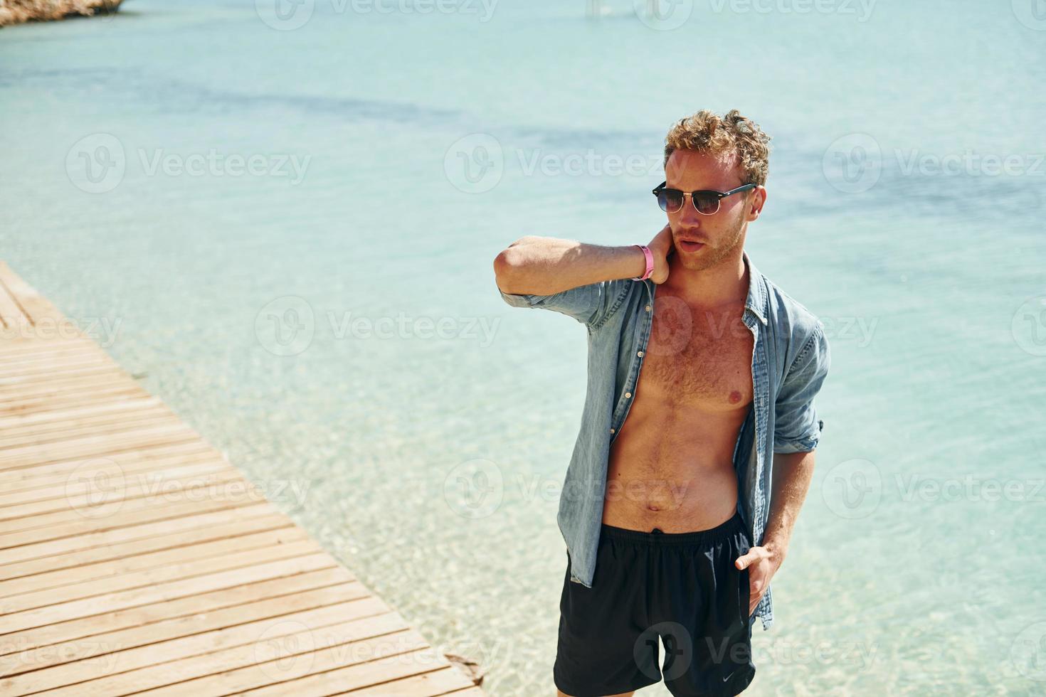 en lunettes de soleil. jeune homme européen passe des vacances et profite de temps libre sur la plage de la mer photo