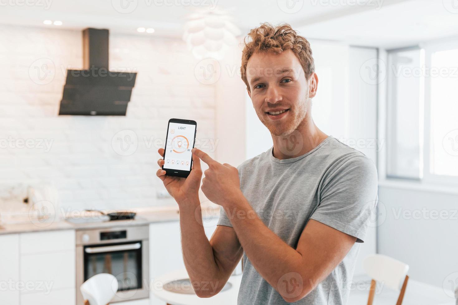 un jeune homme en vêtements décontractés contrôle à l'intérieur la technologie de la maison intelligente photo