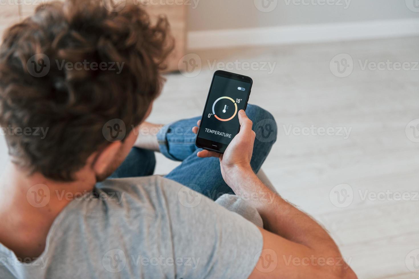 est assis et tient le téléphone dans les mains. vue arrière d'un homme adulte qui contrôle à l'intérieur la technologie de la maison intelligente photo