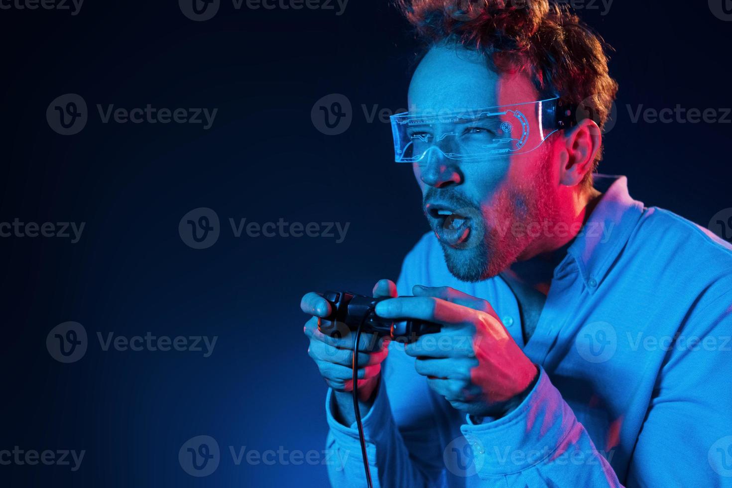 joue au jeu en utilisant le contrôleur. éclairage au néon. jeune homme européen est dans le studio sombre photo