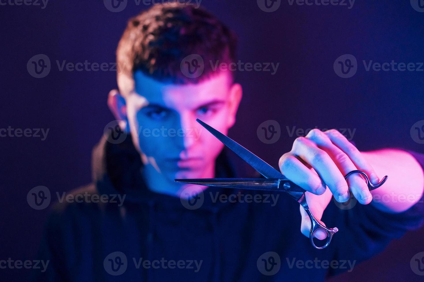 tient des ciseaux. jeune coiffeur avec équipement de travail debout dans le studio avec éclairage au néon photo