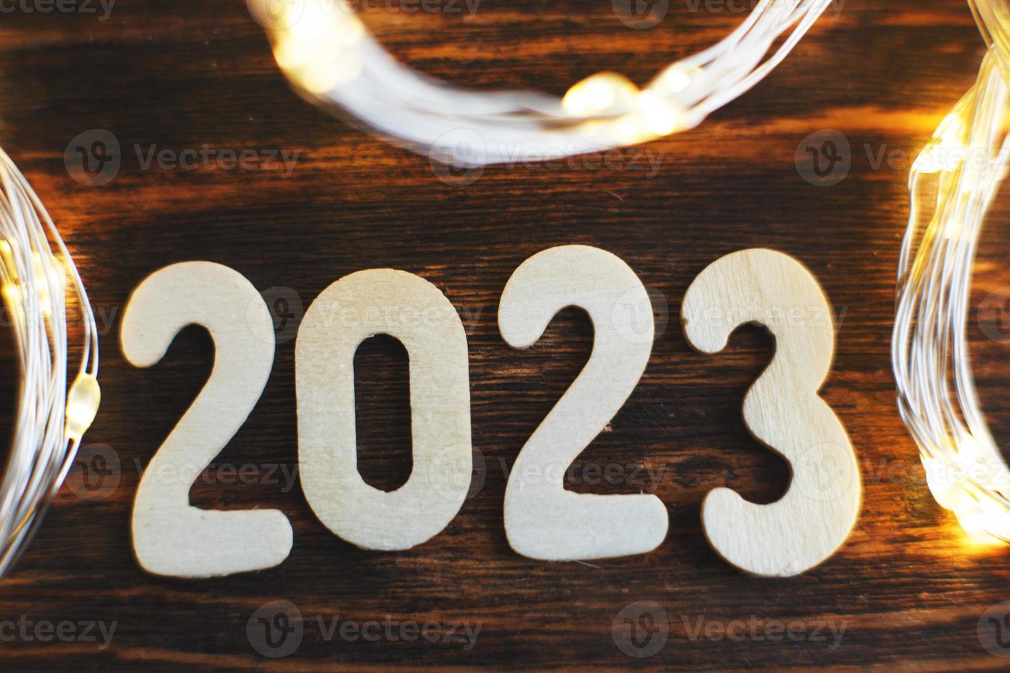 numéro en bois 2023 sur fond de bois brillant de noël. avec guirlande dorée scintillante photo