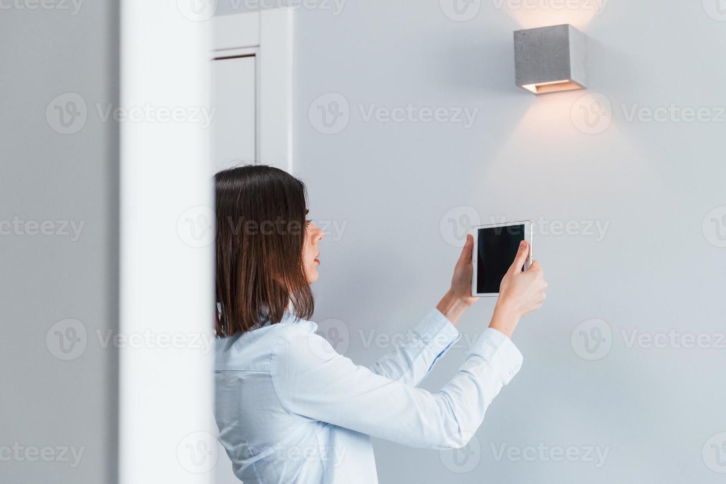 commuter l'éclairage. la jeune femme est à l'intérieur dans la chambre de la maison intelligente pendant la journée photo