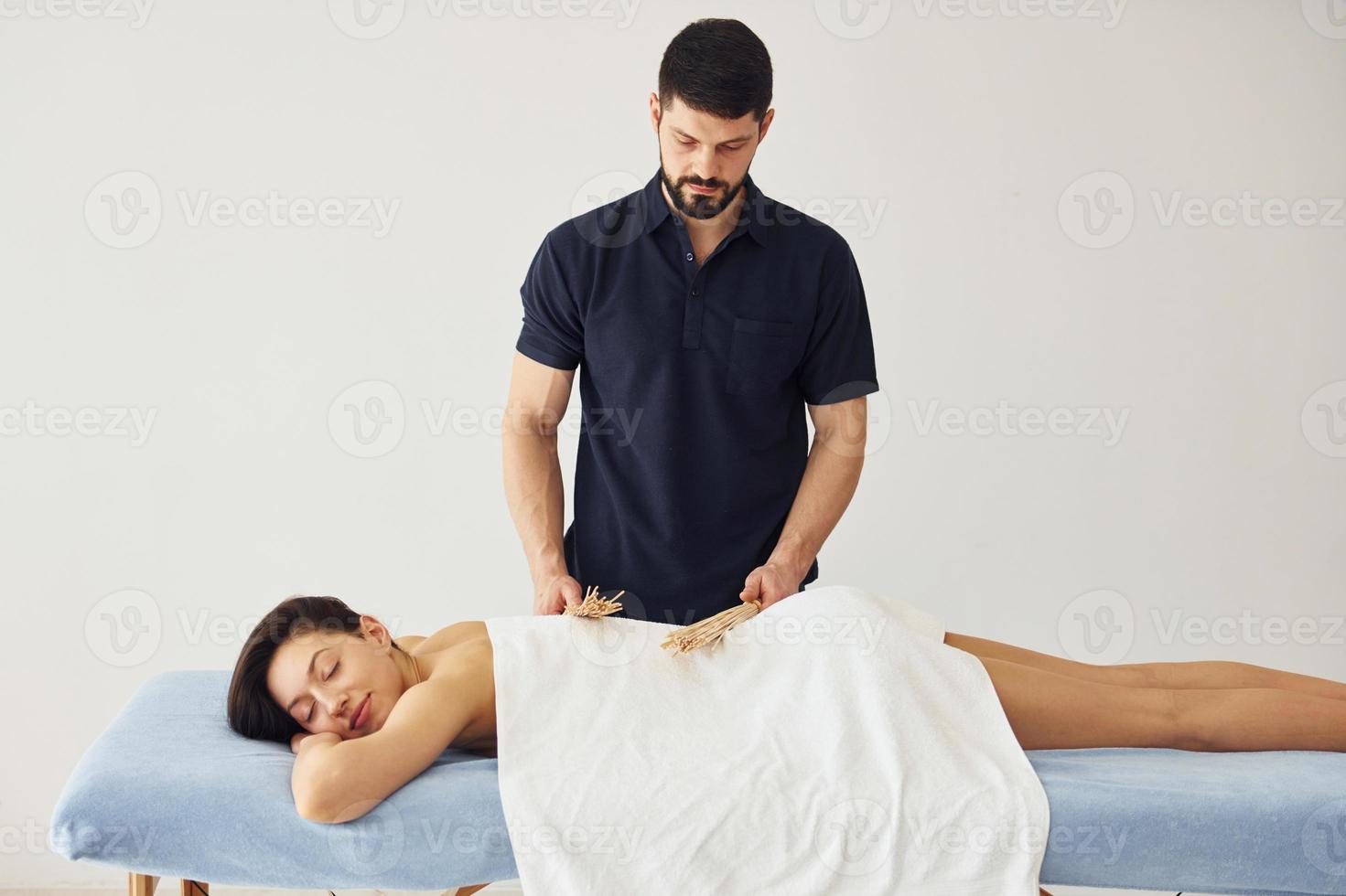 guy utilise des bâtons spéciaux. jeune femme est allongée quand un homme fait un massage de son corps au spa photo