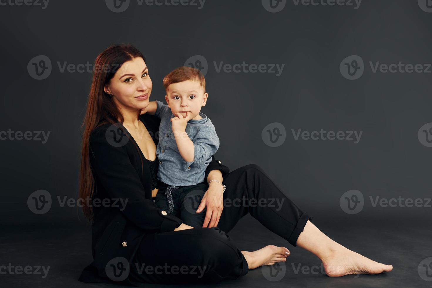 assis sur le sol. mère en vêtements noirs élégants est avec son petit fils dans le studio photo