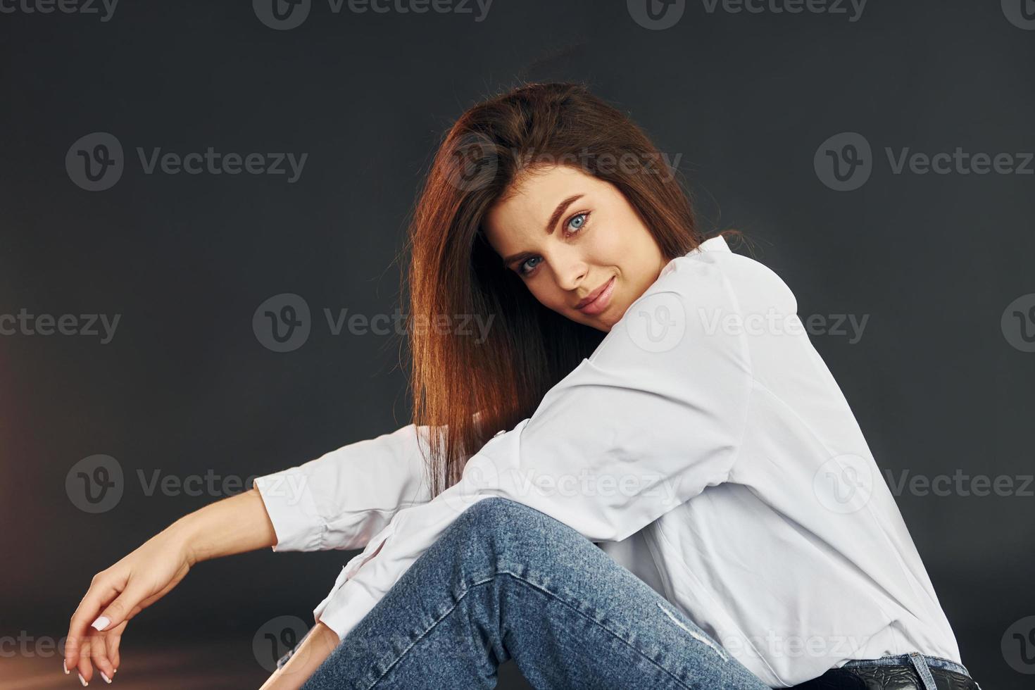 est assis sur le sol. belle jeune femme pose pour la caméra dans le studio photo