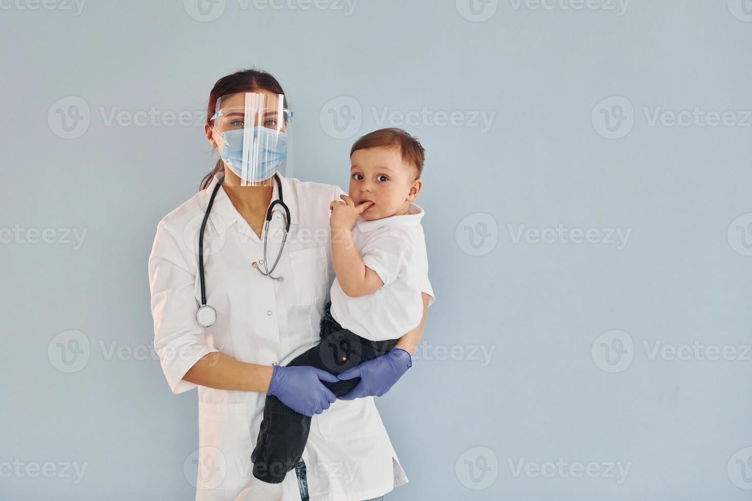 jeune infirmière en blouse blanche et avec stéthoscope tient le petit garçon dans les mains photo