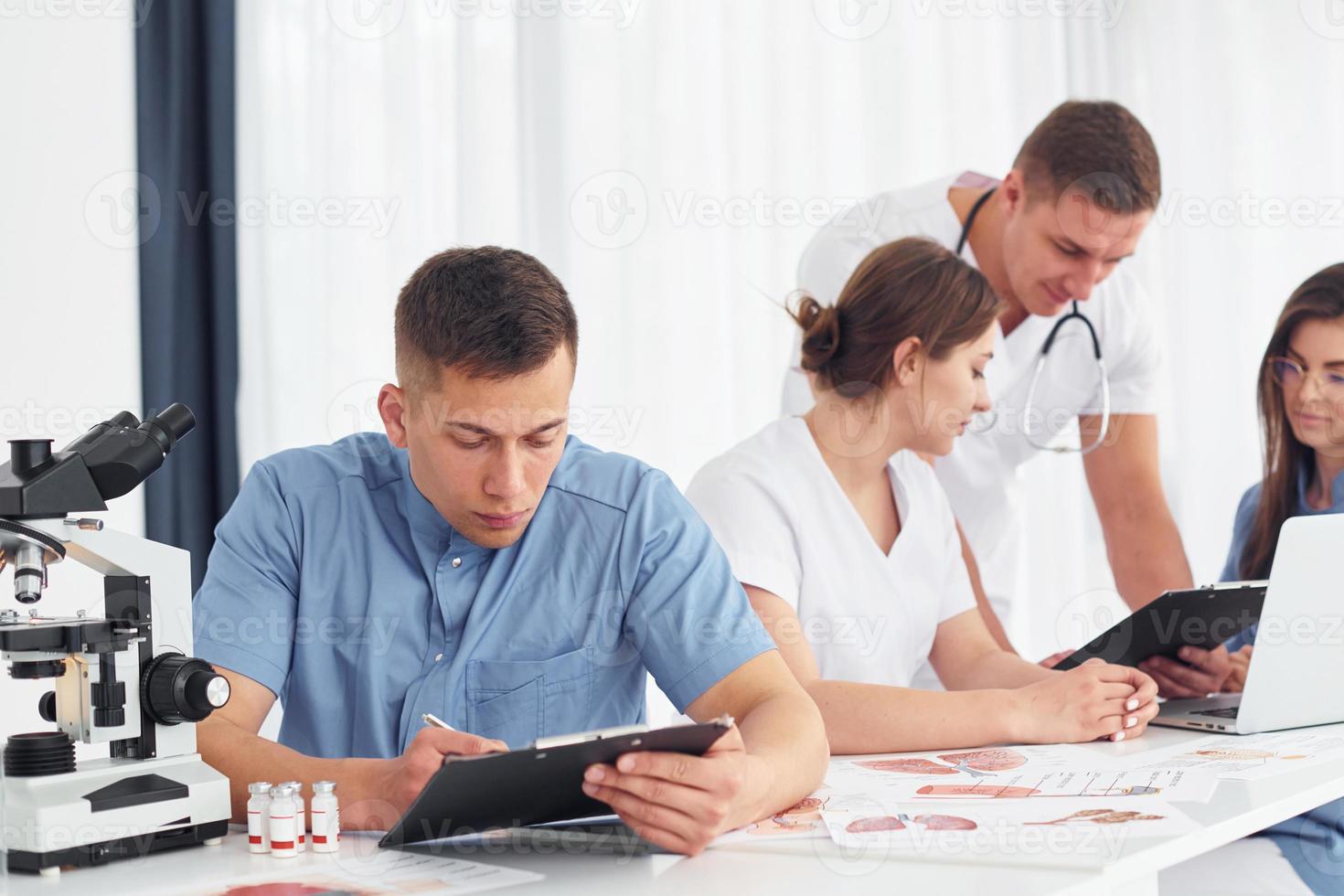 à l'aide d'un microscope. groupe de jeunes médecins travaille ensemble dans le bureau moderne photo