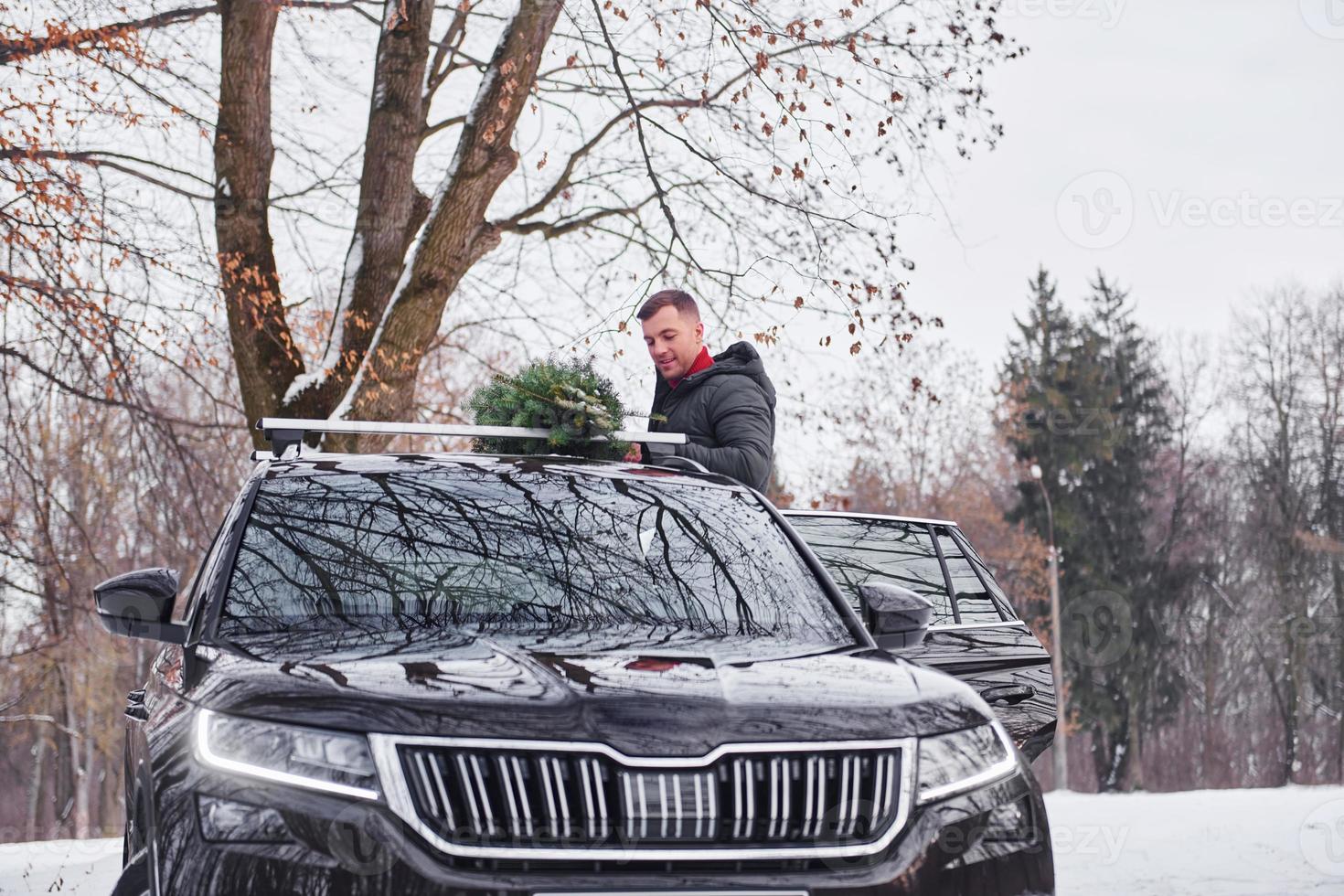 préparer le week-end. l'homme avec un petit sapin vert est à l'extérieur près de sa voiture. conception de vacances photo