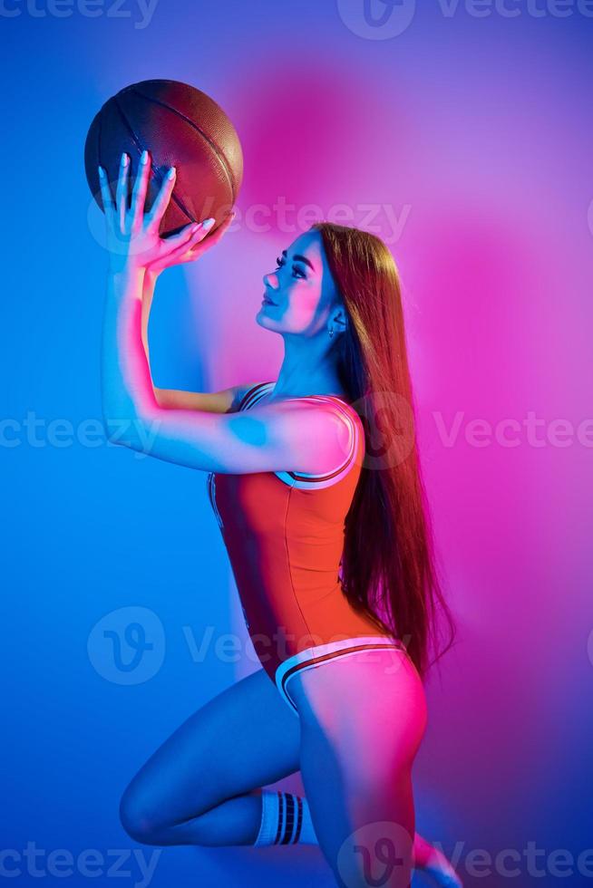 tient le ballon. jeune femme à la mode debout dans le studio avec néon photo