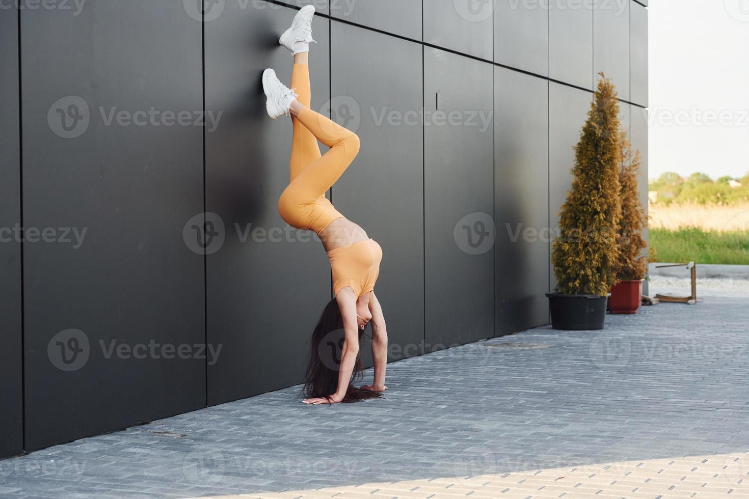 faire le poirier en utilisant le mur. jeune femme en vêtements de sport a une séance de fitness à l'extérieur photo