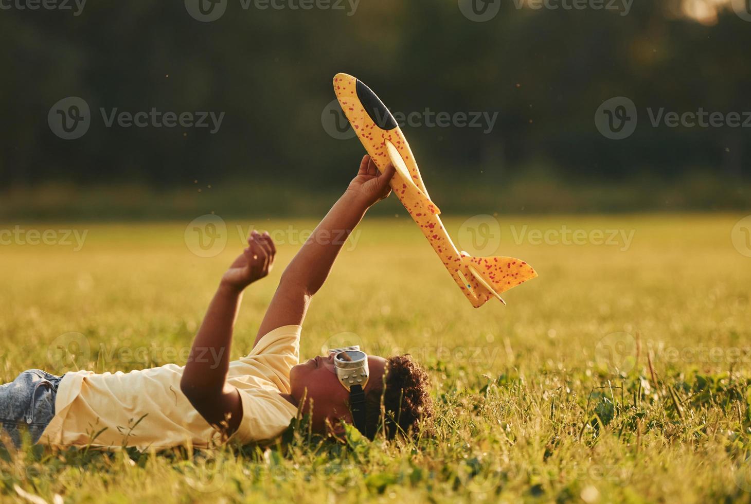 fixant avec avion jouet sur l'herbe. un enfant afro-américain s'amuse sur le terrain pendant la journée d'été photo