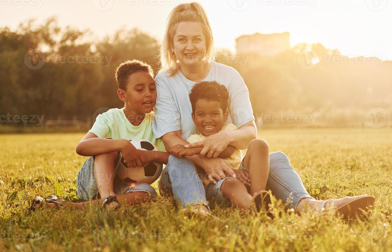 une femme adulte est assise avec deux enfants noirs sur le terrain pendant la journée d'été photo