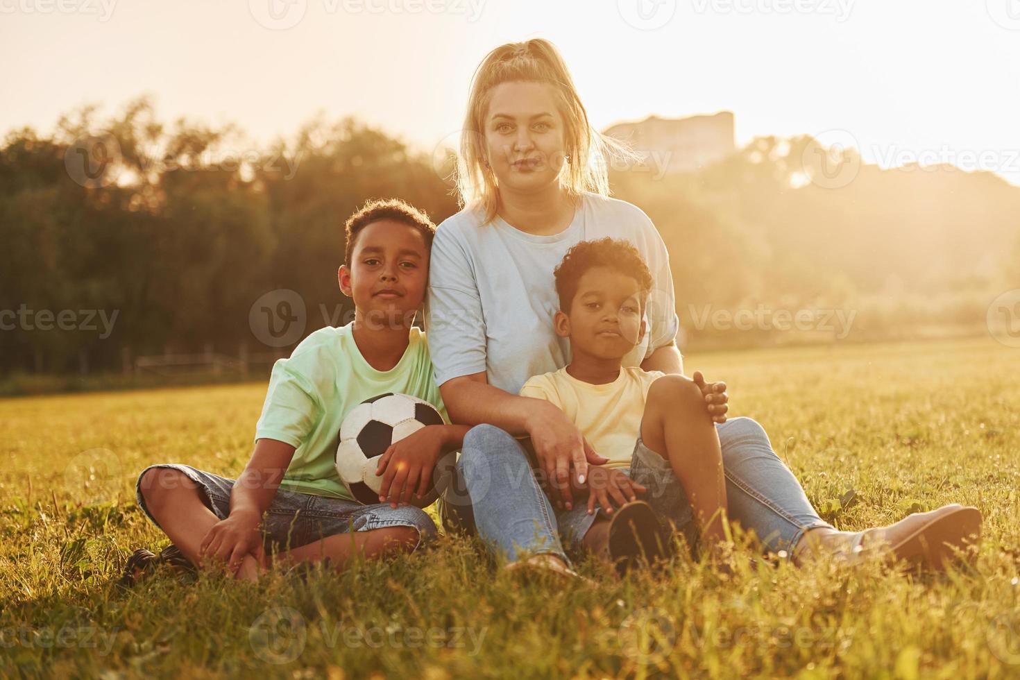 une femme adulte est assise avec deux enfants noirs sur le terrain pendant la journée d'été photo