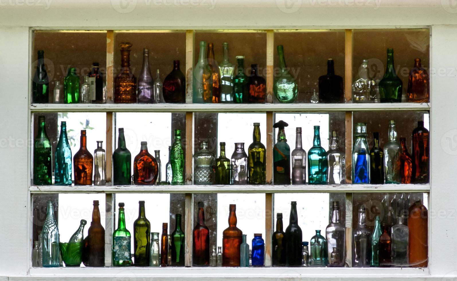 de nombreuses bouteilles en verre colorées vides affichées à l'intérieur d'une fenêtre photo