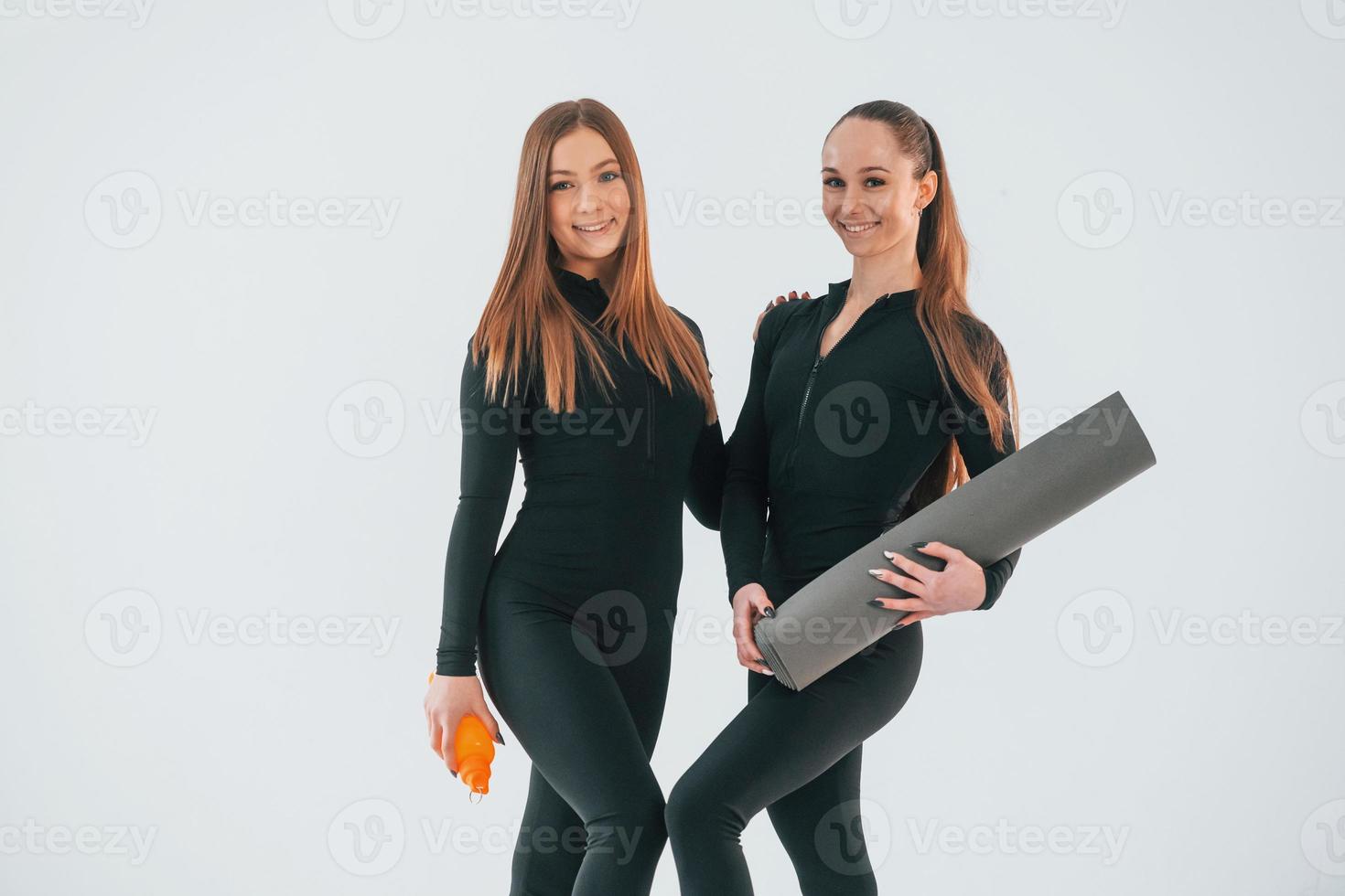 tapis de maintien. deux jeunes femmes en vêtements sportifs sont ensemble à l'intérieur sur fond blanc photo