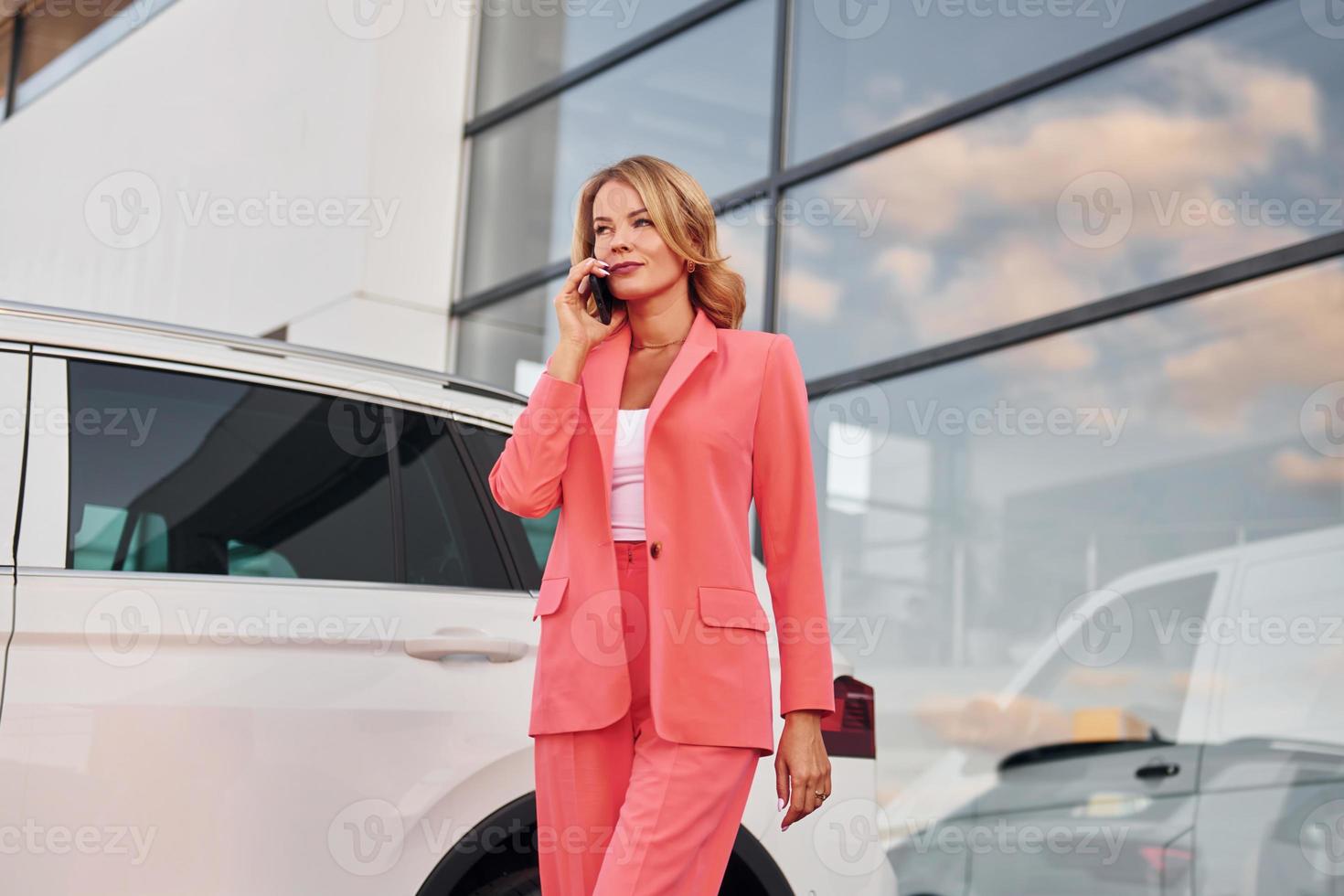 avoir une conversation par téléphone. femme en tenue de soirée debout à l'extérieur avec un téléphone dans les mains et près de la voiture photo