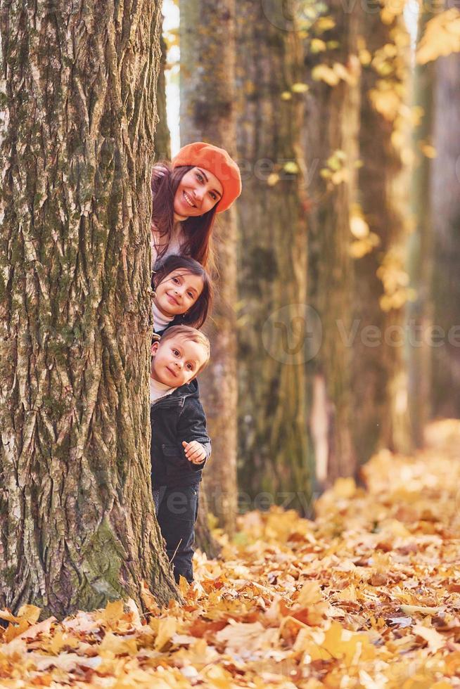 caché derrière un arbre. mère avec son petit fils et sa fille s'amuse dans le parc d'automne photo