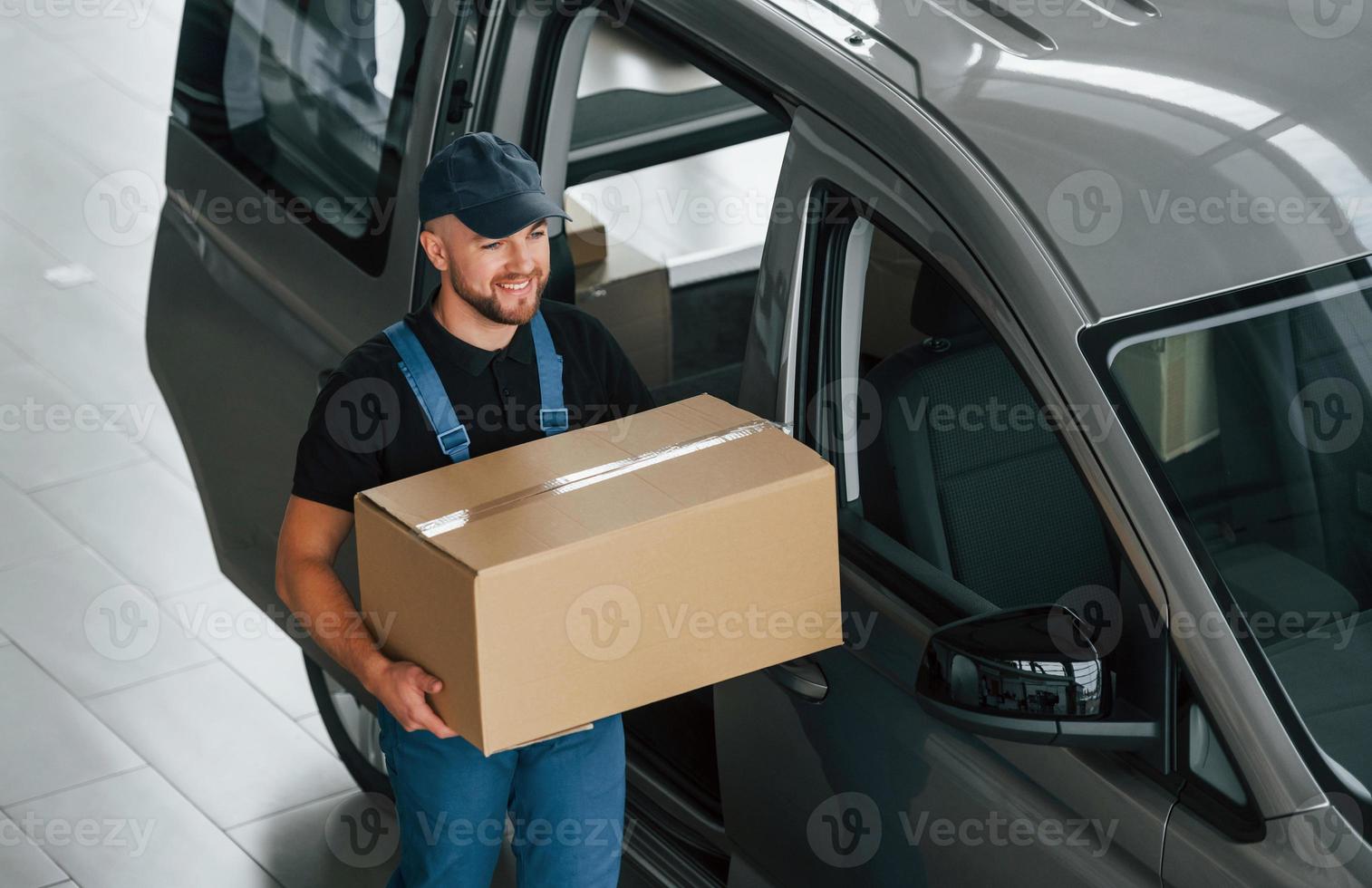 dans des vêtements de couleur bleue. livreur en uniforme est à l'intérieur avec voiture et avec commande photo