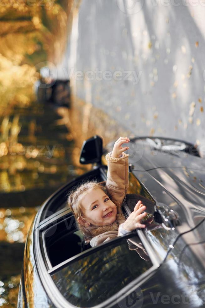 petite fille assise dans l'automobile noire et regardant par la fenêtre photo