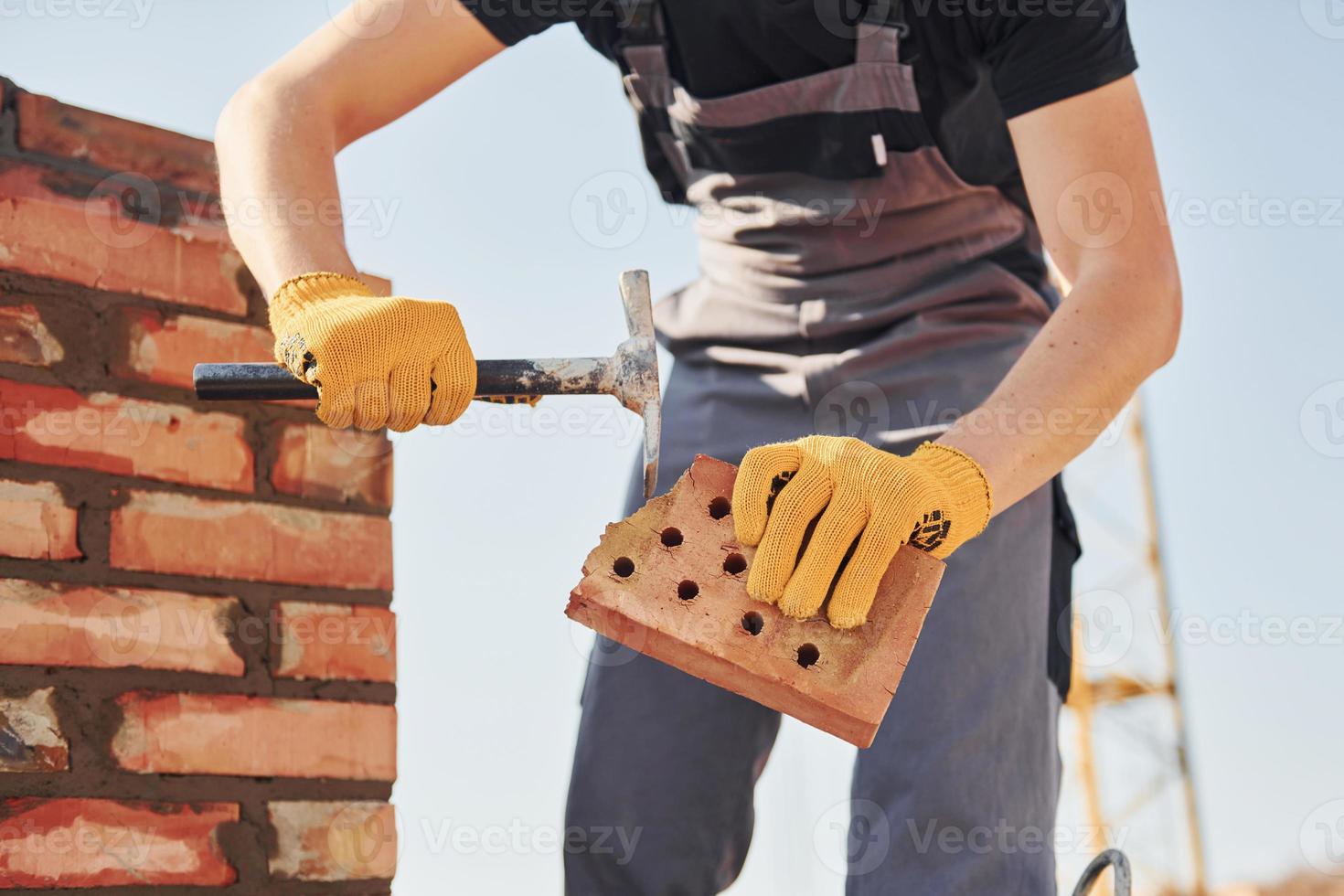 tenant une brique et utilisant un marteau. ouvrier du bâtiment en uniforme et équipement de sécurité a un travail sur le bâtiment photo