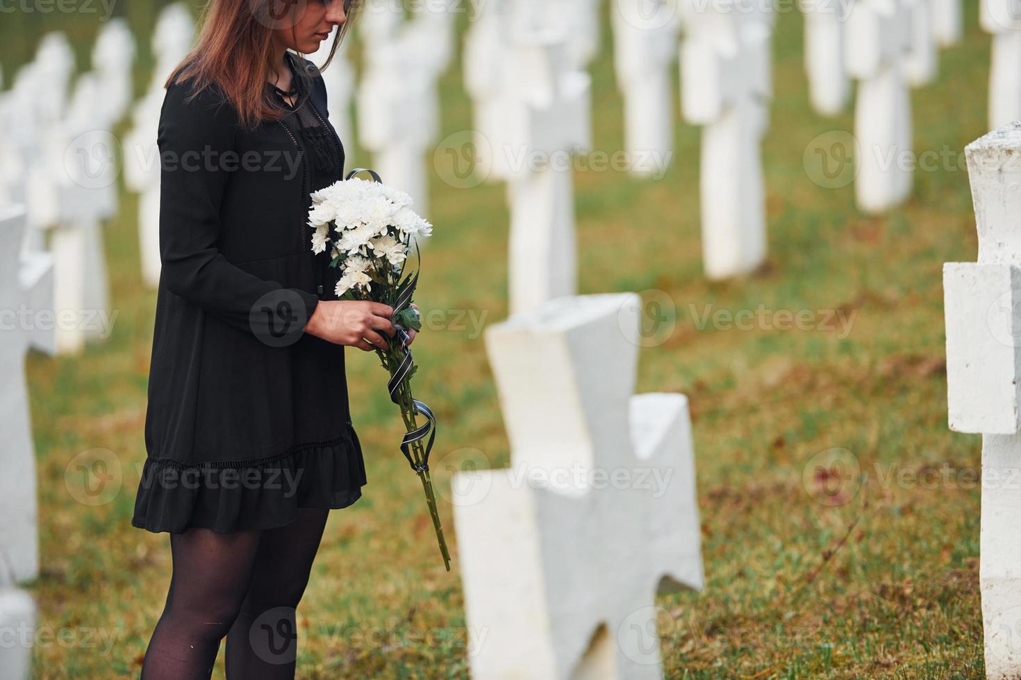 vue particulaire. jeune femme en vêtements noirs visitant le cimetière avec de nombreuses croix blanches. conception des funérailles et de la mort photo