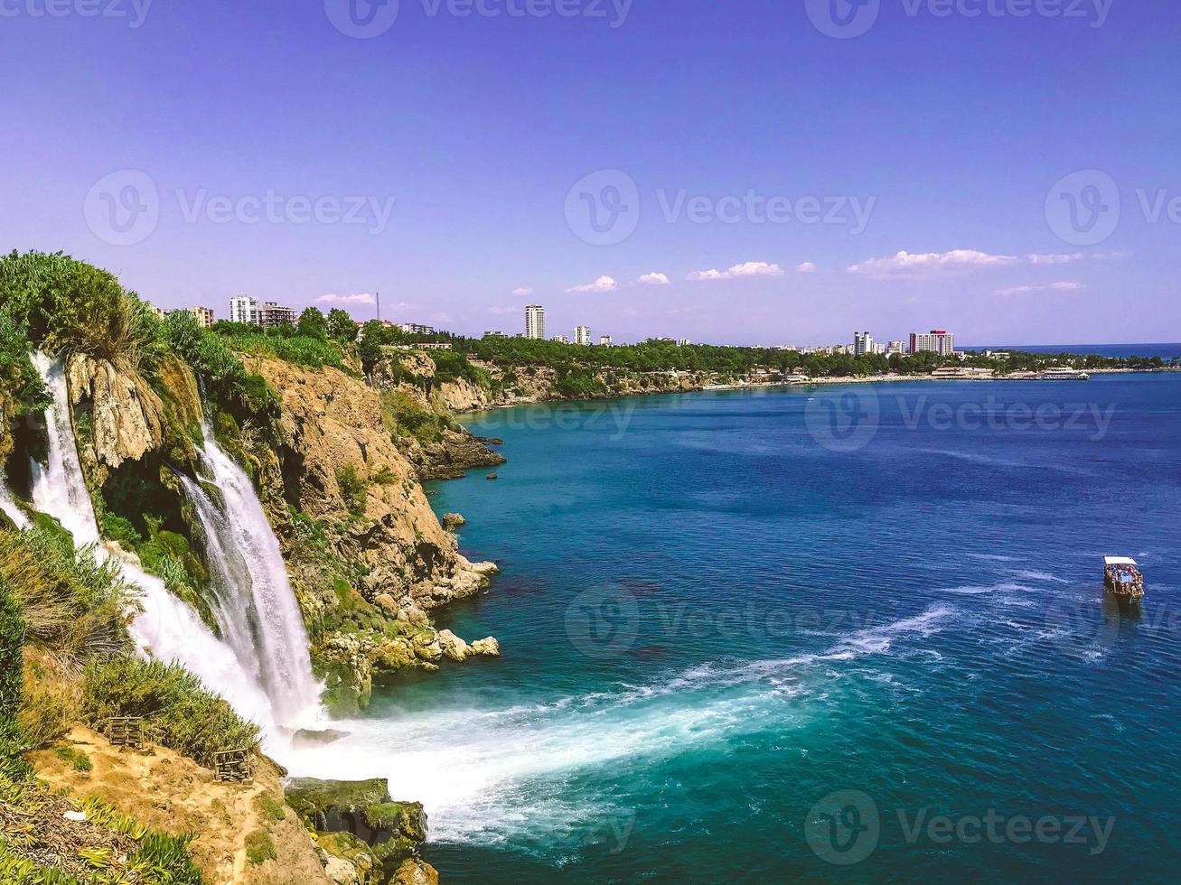 cascade de la mer. un grand bateau avec des touristes flotte dans la mer. mousse blanche d'eau de mer. montagne de pierre avec des montagnes vertes et des plantes photo